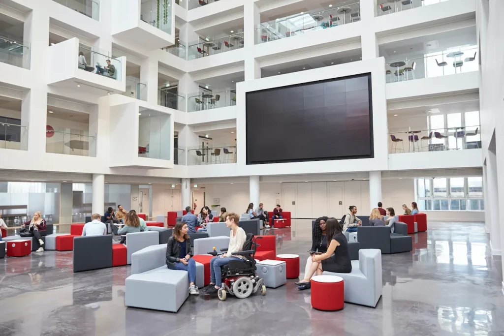 students-socialising-under-av-screen-in-atrium-at-university